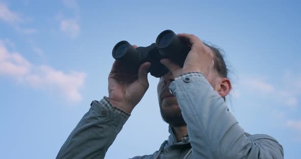 Low Angle View of Traveler Looking Into Field-glass on Blue Sky Background Slow Motion. Serious Man