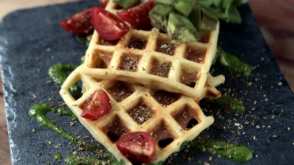 Fresh baked Belgian waffles with arugula, tomatoes and avocado on black a plate. Savory waffles