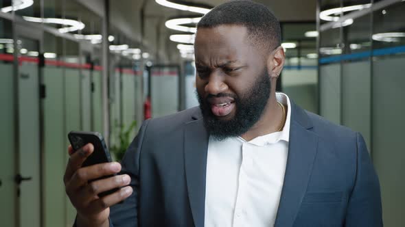 Confused African American Businessman Looks Into a Smartphone