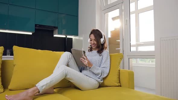 Likable Smiling Young Woman with Wavy Hair and Dressed in Casual Clothes Sitting on the Sofa