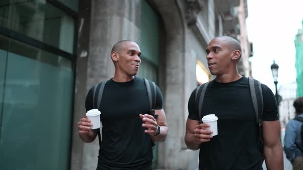 Two smiling bald African brothers talking and walking with cups of coffee on the street