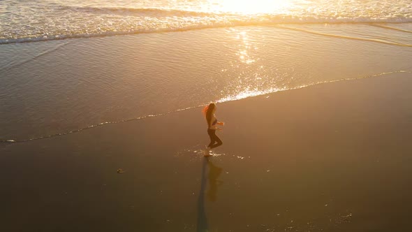 Aerial shot of fit asian woman jogging on the beach at sunset