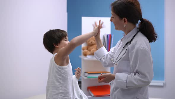 Side View Positive Pediatrician and Patient Gesturing Highfive Hugging in Hospital Indoors