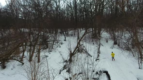 Male Fit Sportsman in Yellow Coat Running up the Hill in Winter Forest