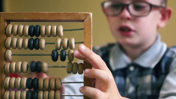 Caucasian boy of 7-8 years old wearing glasses learns to count on the abacus. Accounting theme perfo