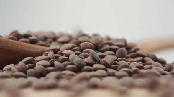 Raw brown uncooked lentils fall into a wooden spoon