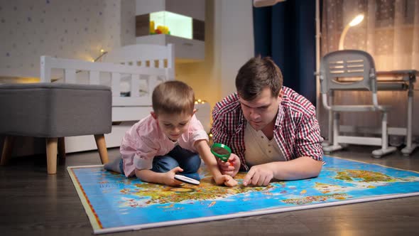 Young Father with Little Son Exploring and Looking on Map Through Magnifying Glass