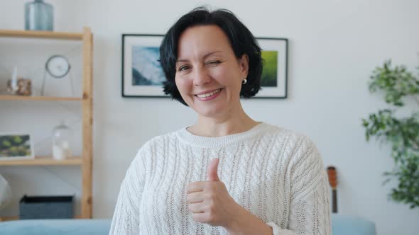 Portrait of Attractive Adult Woman Showing Thumbsup Hand Gesture and Winking Indoors at Home