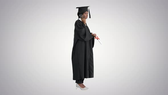 African American Female Student in Graduation Robe Talking on the Phone on Gradient Background