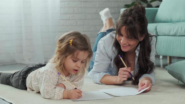 Mom and Daughter Lying on Carpet on the Floor Drawing on Paper Together