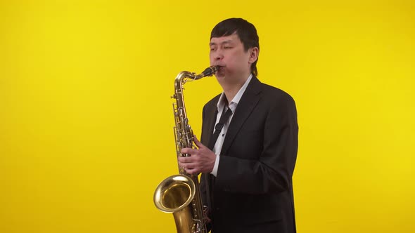 Male musician in suit plays a saxophone on a yellow background. Man plays the saxophone
