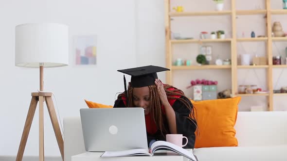 Female Student Wearing Cap and Gown Has Online Talk at Table with Computer at Home Room Spbi