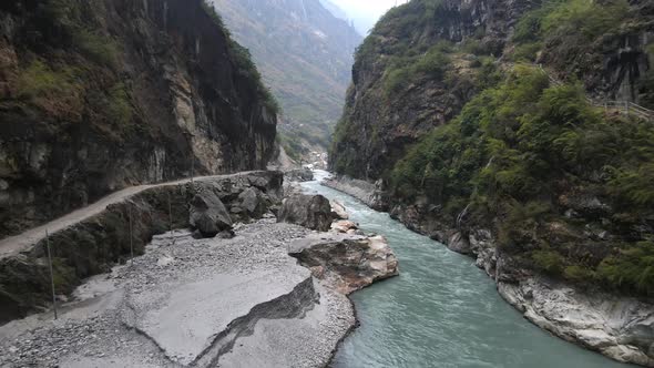 Flying over river deep in a canyon with dirt road following