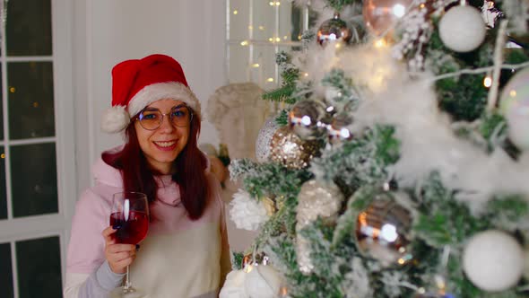Dreamy Woman with Wine Near Christmas Tree Looking Away