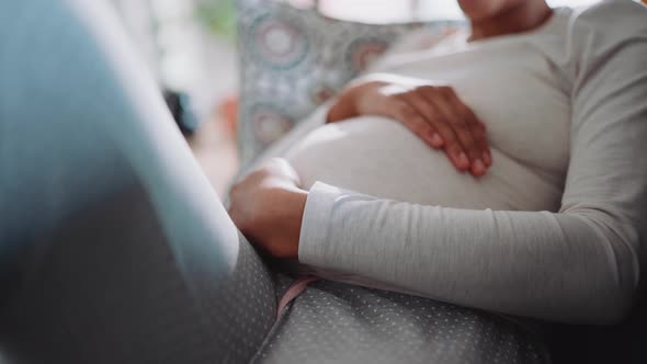 African pregnant woman strokes her belly on the couch