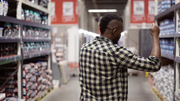 Funny Guy Dances Gesturing in Hardware Goods Store Between Stacks Rear View