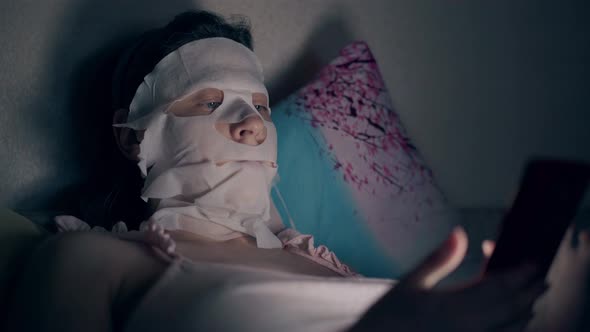 Girl in Pink Top with White Skincare Mask Lies on Pillow