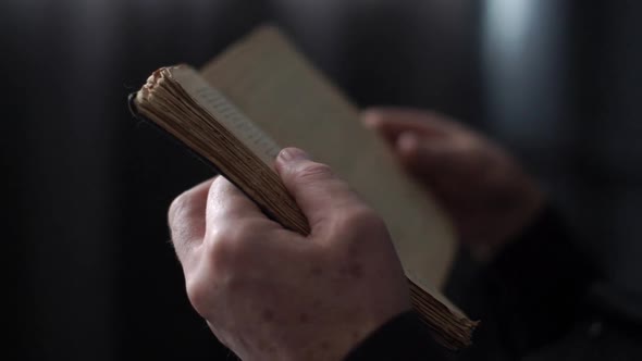 Closeup Hands of Unrecognizable Mature Adult Man Reading Older Book and Flipping Pages in Dark Room