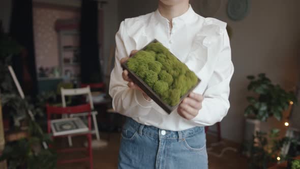 A Pretty Young Girl Demonstrates a Panel in a Wooden Frame Made of Bunches of Decorative Moss for