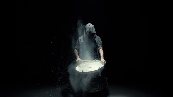 Hooded Man Beats Drum with Flour