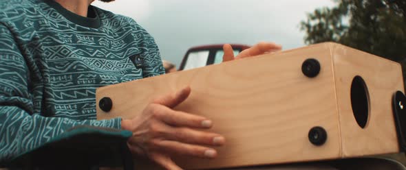 Young man with glasses hand drums on a wooden box