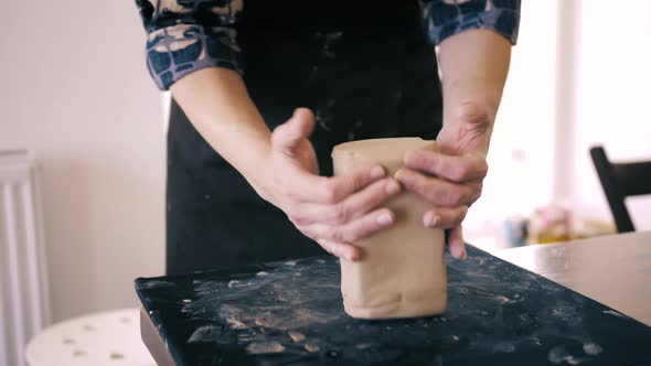 Female hands crumple and roll out piece of clay on table, front view, closeup. Potter prepares clay