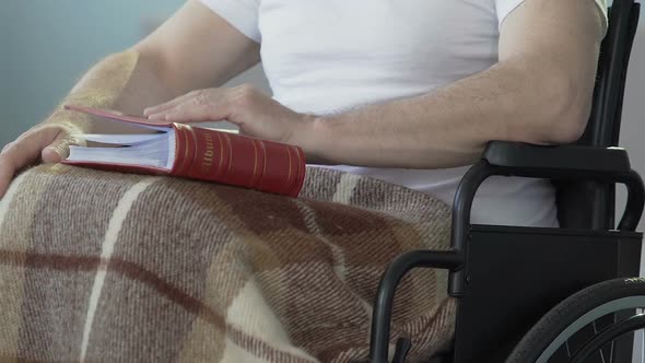 Male sitting wheelchair, opening photo album to look at pictures, past memories