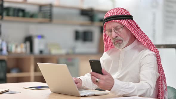 Senior Old Arab Businessman Working on Laptop and Smartphone in Caf� 