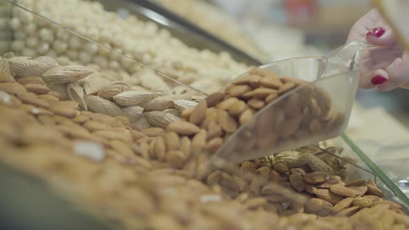 Hand of Unrecognizable Caucasian Woman Taking Healthful Nuts From Grocery Shelf. Unknown Female