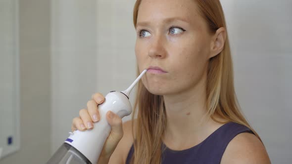 A Young Woman Uses a Portable Water Flosser Dental Oral Irrigator To Clean Her Teeth. Teeth Care