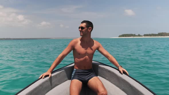 Young Successful Man in Sunglasses Enjoying on the Bow of Boat Floating By Ocean