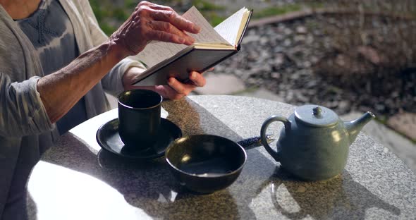 Close up on a woman reading a book and drinking a hot cup of herbal green tea.