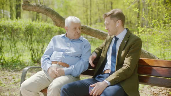 Old Man Is Cheering Up His Son While Sitting on the Bench in the Park