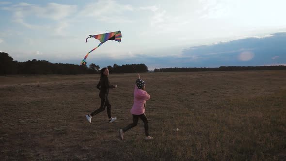 Happy Family Mother and Child Daughter Launch a Kite on Meadow at Sunset. Funny Family Time. Concept