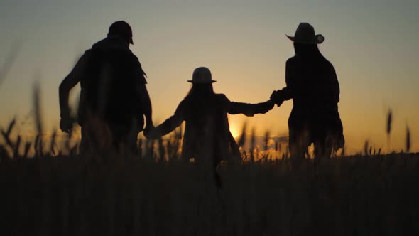 Silhouette Family Farmers Working in a Wheat Field at Sunset. Young Parents with Their Daughter in a