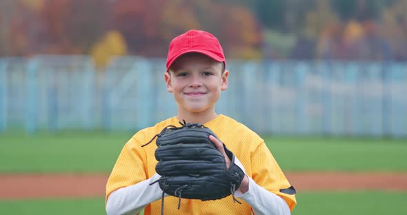 Portrait of a Boy Baseball Player on a Blurry Background, the Pitcher Holds the Ball in His Glove