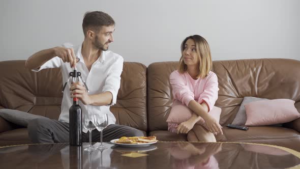 Handsome Man Opening Wine Bottle Using Corkscrew While His Wife Sitting Near. Happy Married Couple