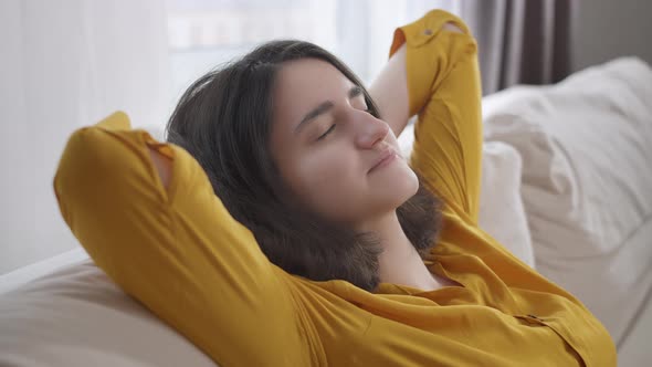 Happy Girl Relaxing on the Couch with Closed Eyes Hands Behind Her Head Sitting at Home