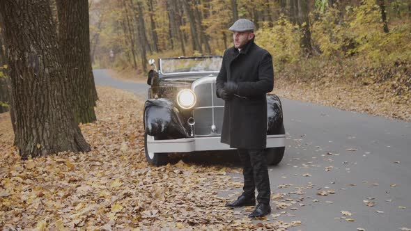 Portrait of Handsome Gentleman Corrects His Coat in Autumn Park at Retro Car