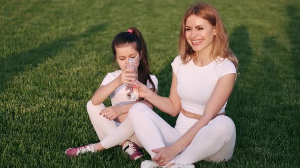 Mother and Daughter Are Drinking Water on the Grass