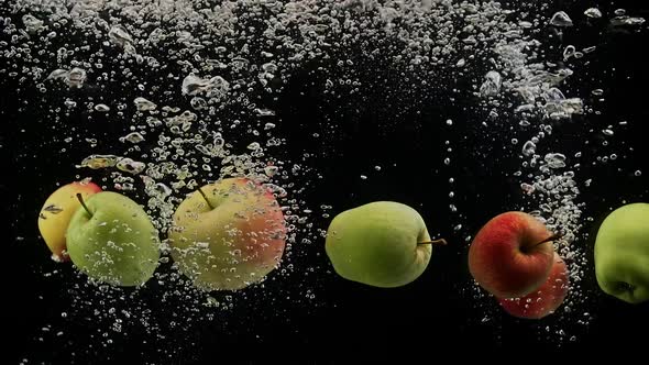 Fresh Apples Green and Red Falling Into Water with Air Bubbles Isolated on Black Background