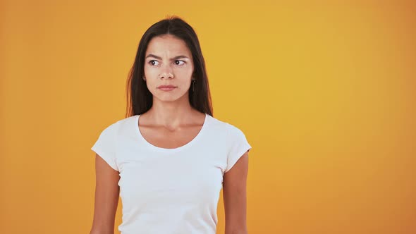 Woman Looking Confused and Surprised Smiling While Posing on Orange Background
