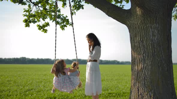 A Young Mother Shakes Her Daughters on a Wooden Rope Swing.