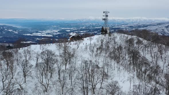 white snow mountain peak in winter at nozawa onsen with skiers and mountain cabin, aerial