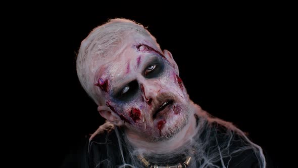 Sinister Man with Horrible Scary Halloween Zombie Makeup in Convulsions Making Faces Trying to Scare