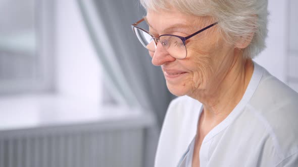 Grey haired old grandmother in glasses looks downward