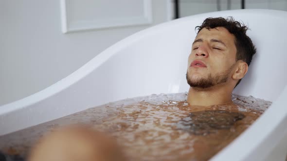 Man Sits with Closed Eyes in the Bath with Ice Cubes for Recovery