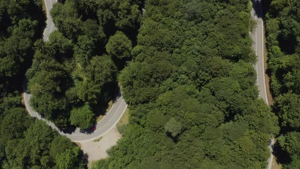 Top down drone shot at a red car which is driving along a curvy road with other cars passing by the