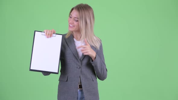 Happy Young Blonde Businesswoman Showing Clipboard and Giving Thumbs Up