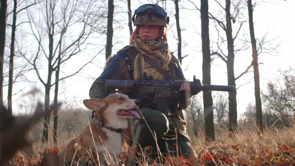 Young Pretty Redhead Woman in Military Uniform Armed with Rifle Playing with Dog